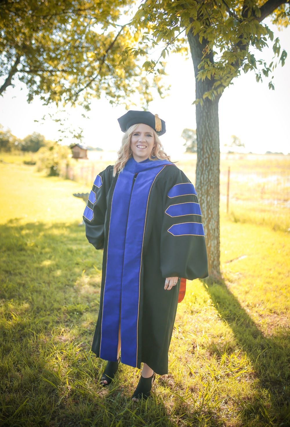 Brandi in doctoral regalia under a tree